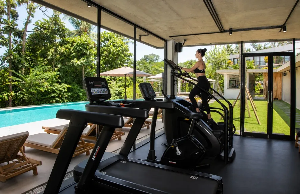 Treadmill and stair climber in the glass-walled gym at Nova Wellness Club in Ubud, next to the pool