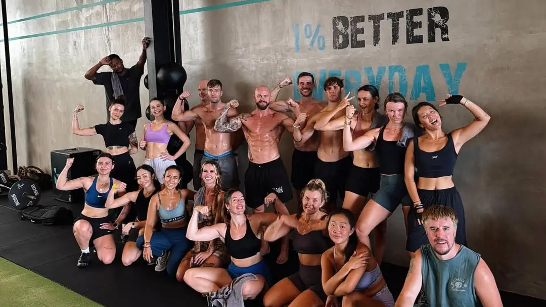 A group class posing after a workout at Threshold Gym in Seseh, in front of a wall painted "1% better everyday"